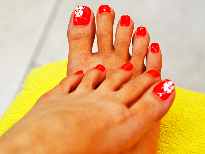 Rote Pediküre an den Füßen. Foto mit Design, Strasssteinen, Mustern, Reiben